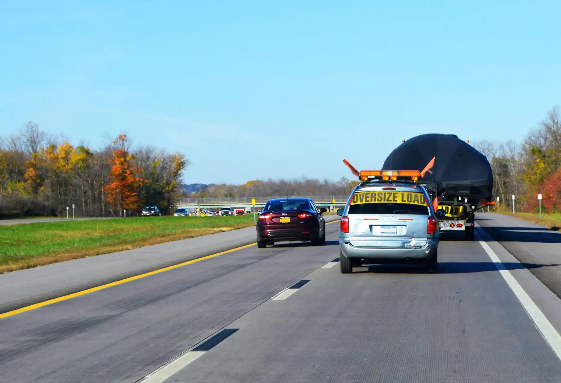 Vehicle towing an oversized load on a highway in clear weather. A vehicle towing an oversized load on a highway with other cars and trees in the background.